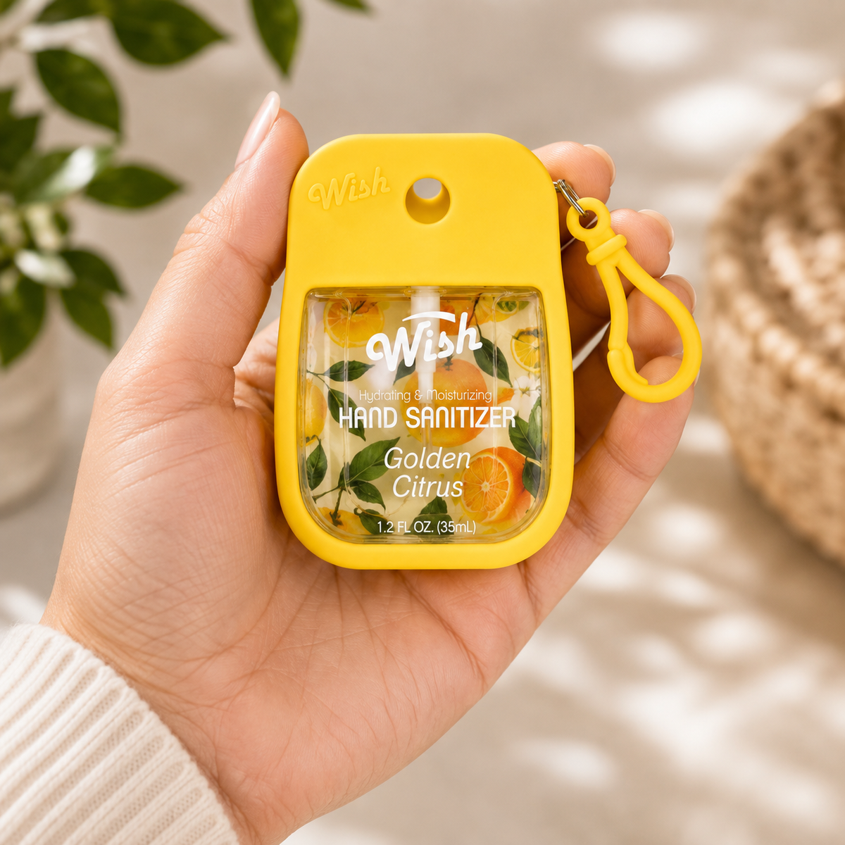 A hand holding a small yellow hand sanitizer bottle with a matching yellow keychain loop. The bottle has a clear front window showing citrus-themed liquid and label text that reads 'wish' and 'Golden Citrus'.