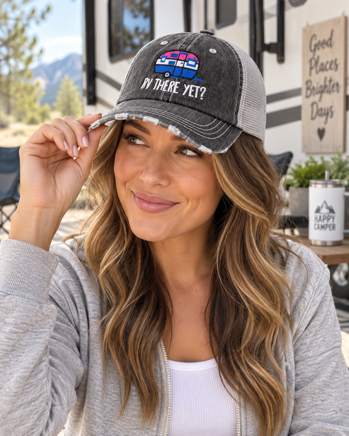 Woman wearing RV There Yet Trucker Hat with distressed black front and gray mesh back tilted up showing pink and blue embroidered camper graphic with white RV There Yet lettering and RV mountain backdrop
