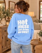 Model showing the white Hot Mess Just Doing My Best back graphic on a light blue sweatshirt, paired with jeans
