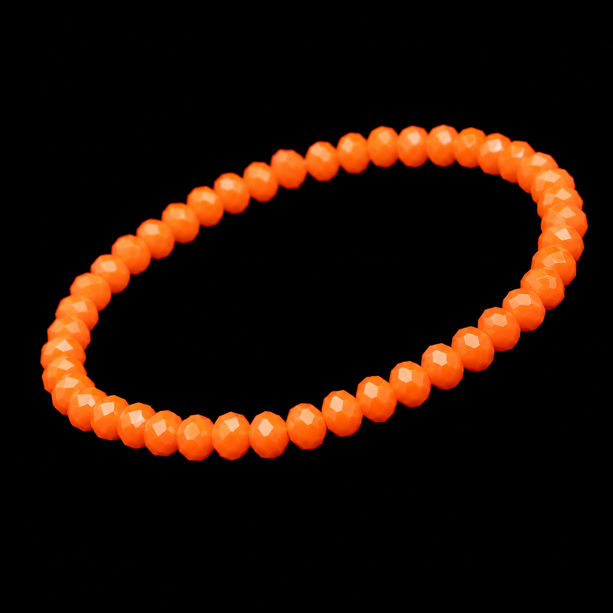 orange faceted bead stretch bracelet shown at an angle on black reflective surface
