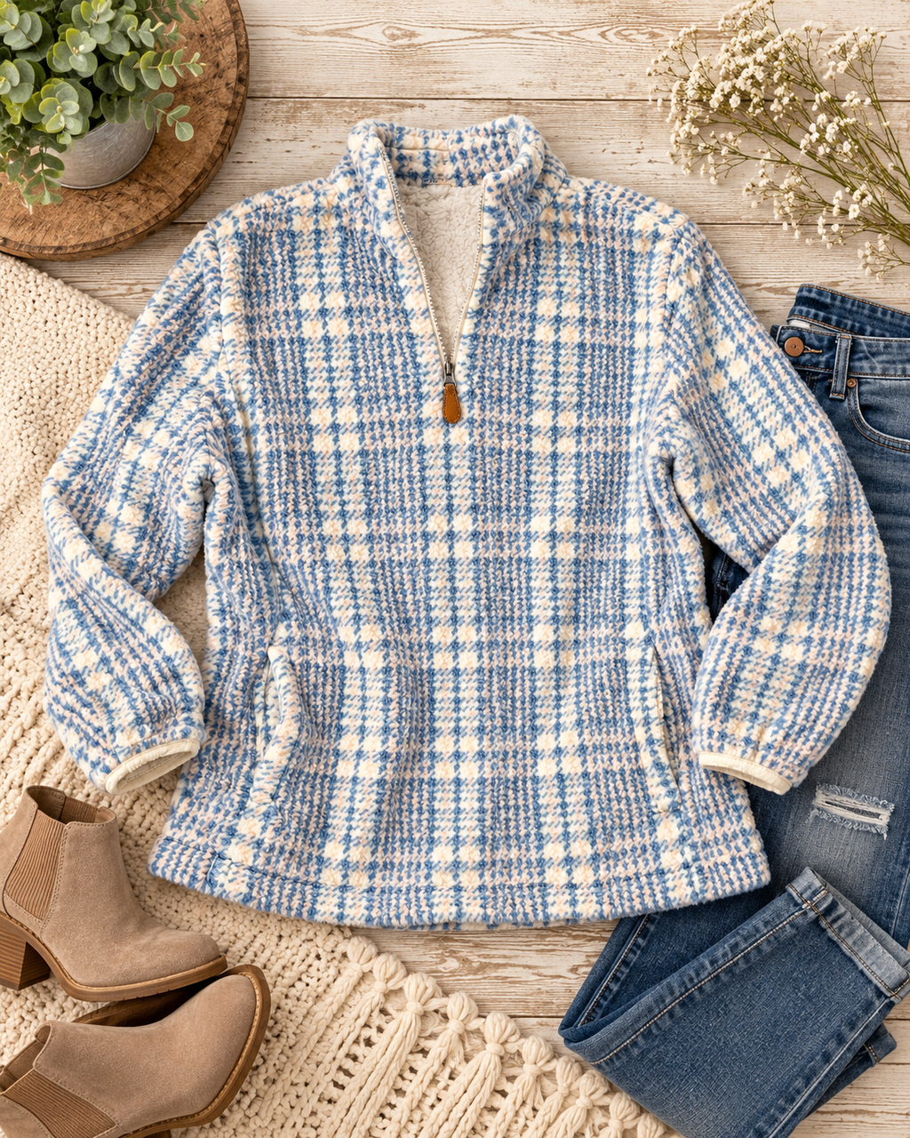 Blue and cream plaid fleece pullover styled with distressed jeans, tan ankle boots, a cream fringed throw, greenery, and flowers on rustic wood
