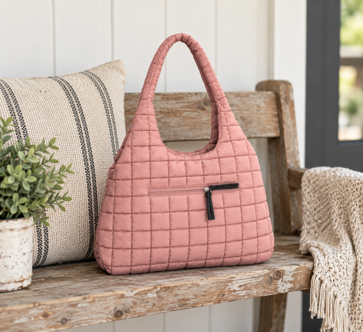 Mauve Quilted Tote Bag displayed on rustic wooden bench showing soft mauve puffer quilted body and front zippered pocket with striped pillow, potted plant, and knit throw in farmhouse porch setting
