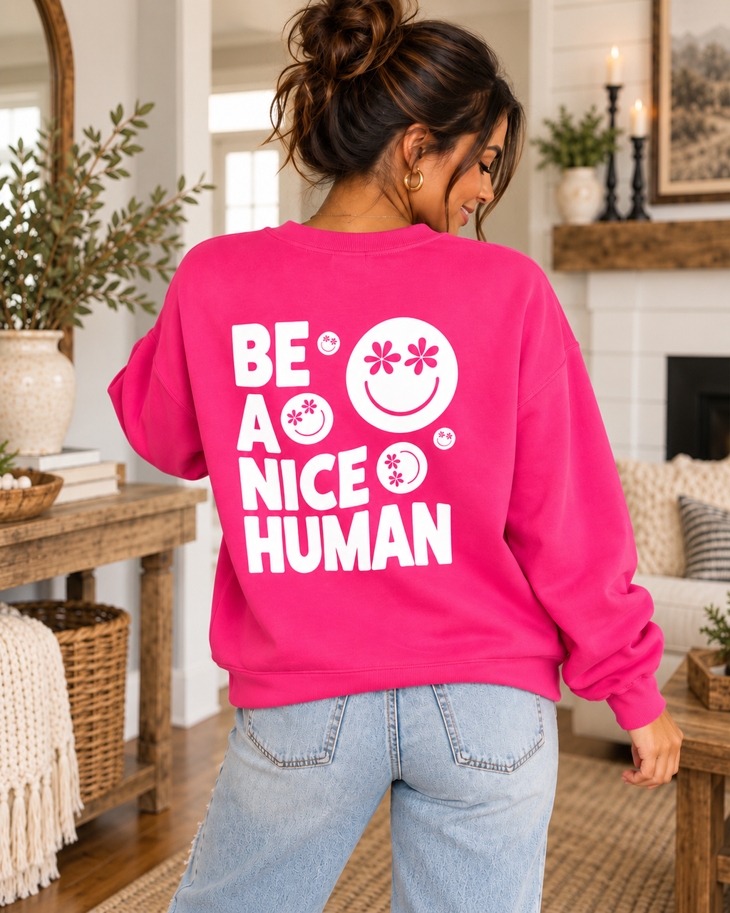 Model showing the white Be a Nice Human back graphic on a hot pink sweatshirt, paired with jeans
