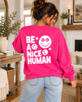 Model showing the white Be a Nice Human back graphic on a hot pink sweatshirt, paired with jeans
