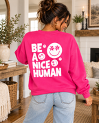 Model showing the white Be a Nice Human back graphic on a hot pink sweatshirt, paired with jeans
