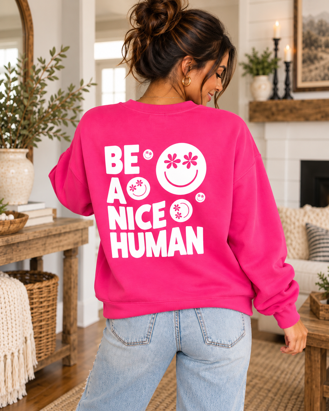 Model showing the white Be a Nice Human back graphic on a hot pink sweatshirt, paired with jeans
