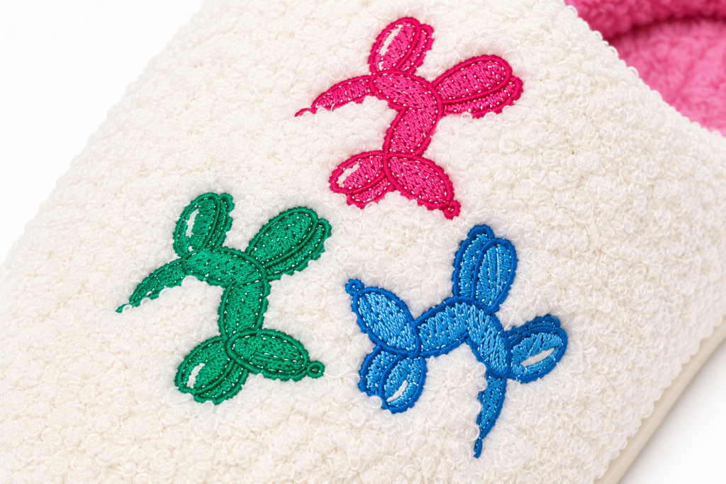 Close-up of colorful embroidered balloon dog accents on Ivory Balloon Dog Fuzzy Slippers showing detailed pink, green, and blue balloon animal designs on soft ivory fuzzy fabric
