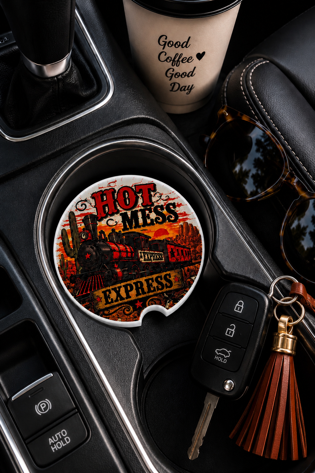 Hot Mess Express ceramic car coaster sitting in vehicle cup holder next to a coffee cup, sunglasses, and car keys — vintage steam train with bold red "Hot Mess Express" lettering
