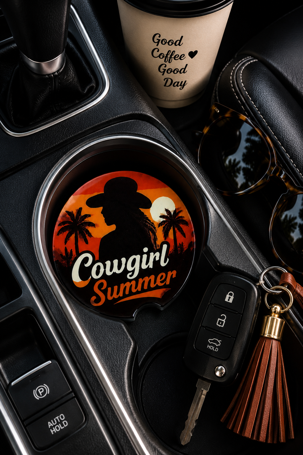 Cowgirl Summer ceramic car coaster sitting in vehicle cup holder next to a coffee cup, sunglasses, and keys — cowgirl silhouette with palm trees and orange sunset design
