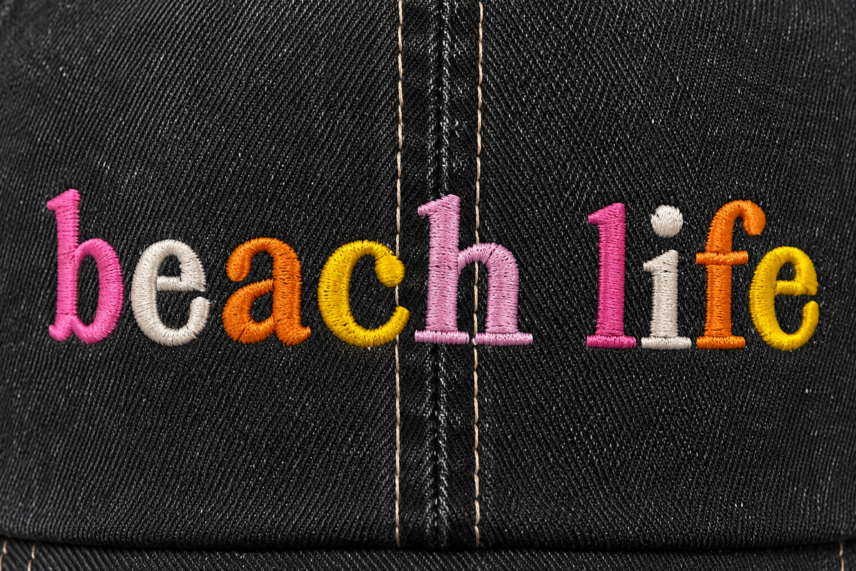 Close-up of multicolor embroidered "Beach Life" lettering on a distressed black trucker hat front panel.
