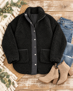 Black sherpa teddy jacket styled with jeans, tan ankle boots, a fringed throw, and greenery on rustic wood
