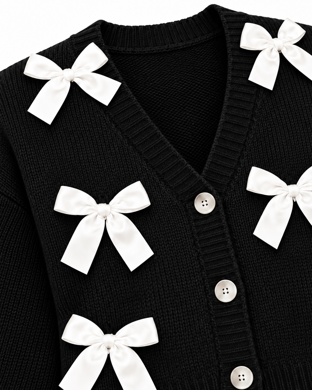 Close-up of Black Satin Bow Knit Cardigan showing deep V-neckline with ribbed trim, pearl dome buttons along button placket, and white satin ribbon bow detail on black ribbed knit on white background
