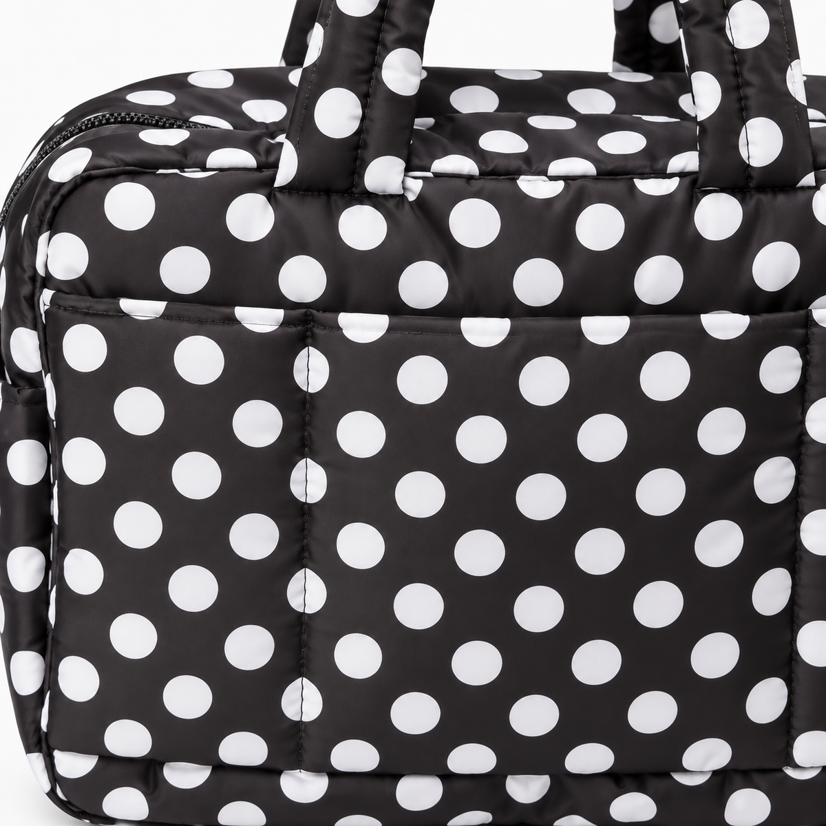 Close-up of Black Polka Dot Shoulder Tote Bag showing black padded quilted fabric texture with bold white polka dots, top zipper closure, and large front slip pocket detail on white background
