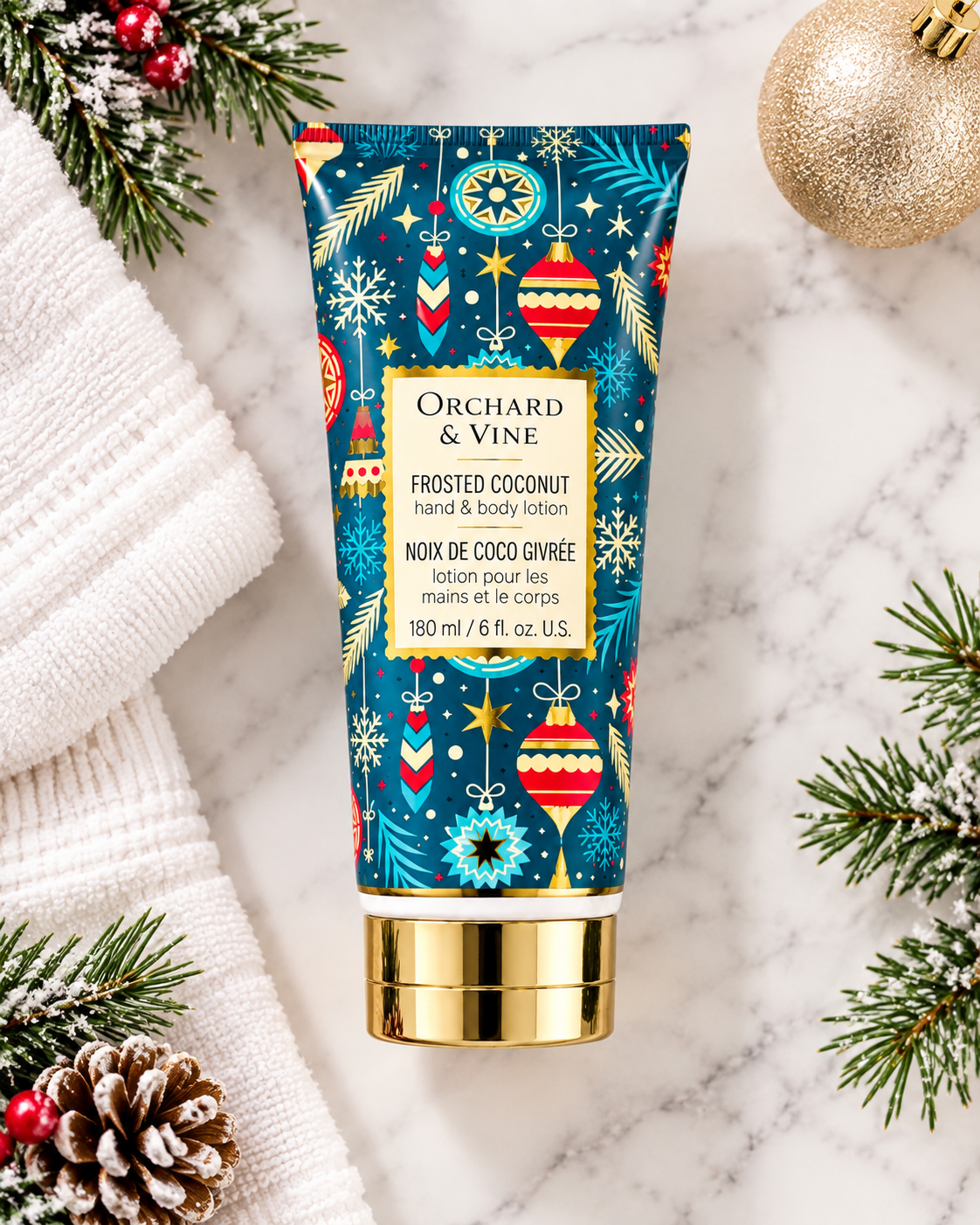 Frosted Coconut hand and body lotion laid flat beside white towels, frosted evergreen branches, pinecones, and a gold Christmas ornament
