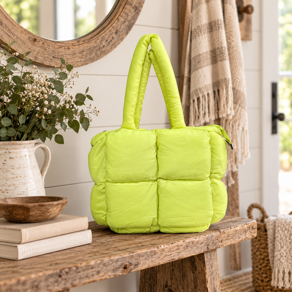 Lime Mini Puffer Tote Bag on rustic wood entryway bench showing bright lime green large-panel puffer quilted nylon and dual tubular puffer handles beside white stoneware pitcher of greenery, wooden bowl, stacked books, and plaid fringe throw against white shiplap wall with round wood mirror
