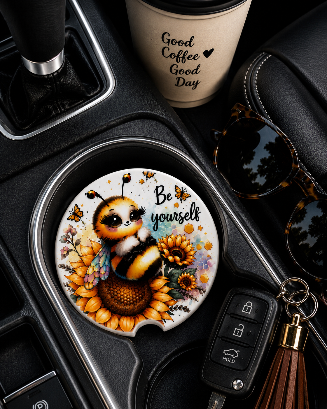Be Yourself ceramic car coaster in cup holder — cute bee and sunflower design, shown in car console with coffee cup and sunglasses
