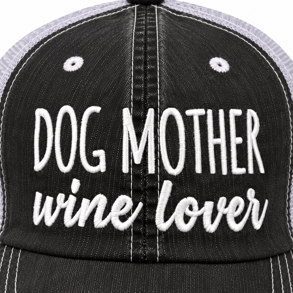 Close-up of white embroidered Dog Mother block lettering and wine lover script on distressed black trucker hat front panel

