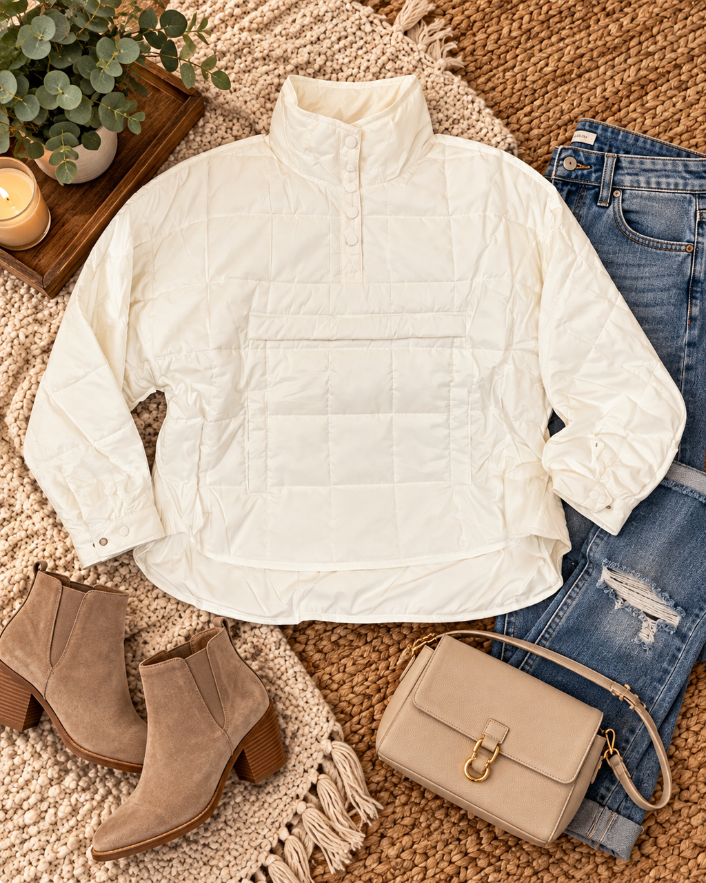White quilted puffer jacket styled on a woven rug with jeans, booties, a tan crossbody bag, eucalyptus, and a candle.
