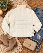White quilted puffer jacket styled on a woven rug with jeans, booties, a tan crossbody bag, eucalyptus, and a candle.
