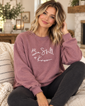 Model wearing the dusty mauve Be Still + Know crewneck sweatshirt with white script lettering and black pants
