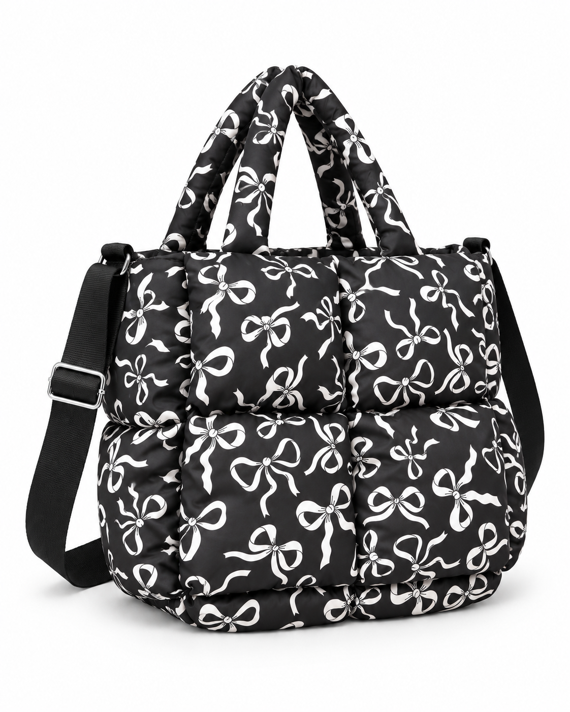 Black Bow Print Puffer Tote three-quarter angle view showing black puffer body with all-over white bow print, dual padded top handles, adjustable black shoulder strap, and silver hardware on white background
