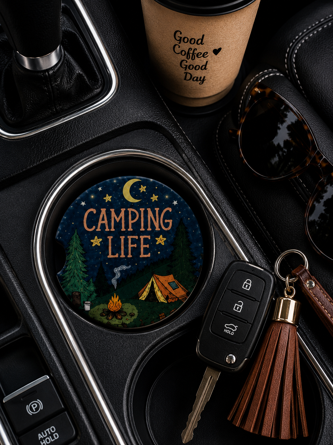 Camping Life ceramic car coaster in cup holder — campfire, orange tent, pine trees, and starry night sky design, shown in car console with coffee cup and sunglasses
