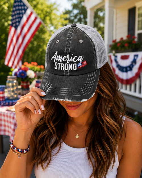 Woman wearing America Strong distressed trucker hat with American flag background at Fourth of July celebration