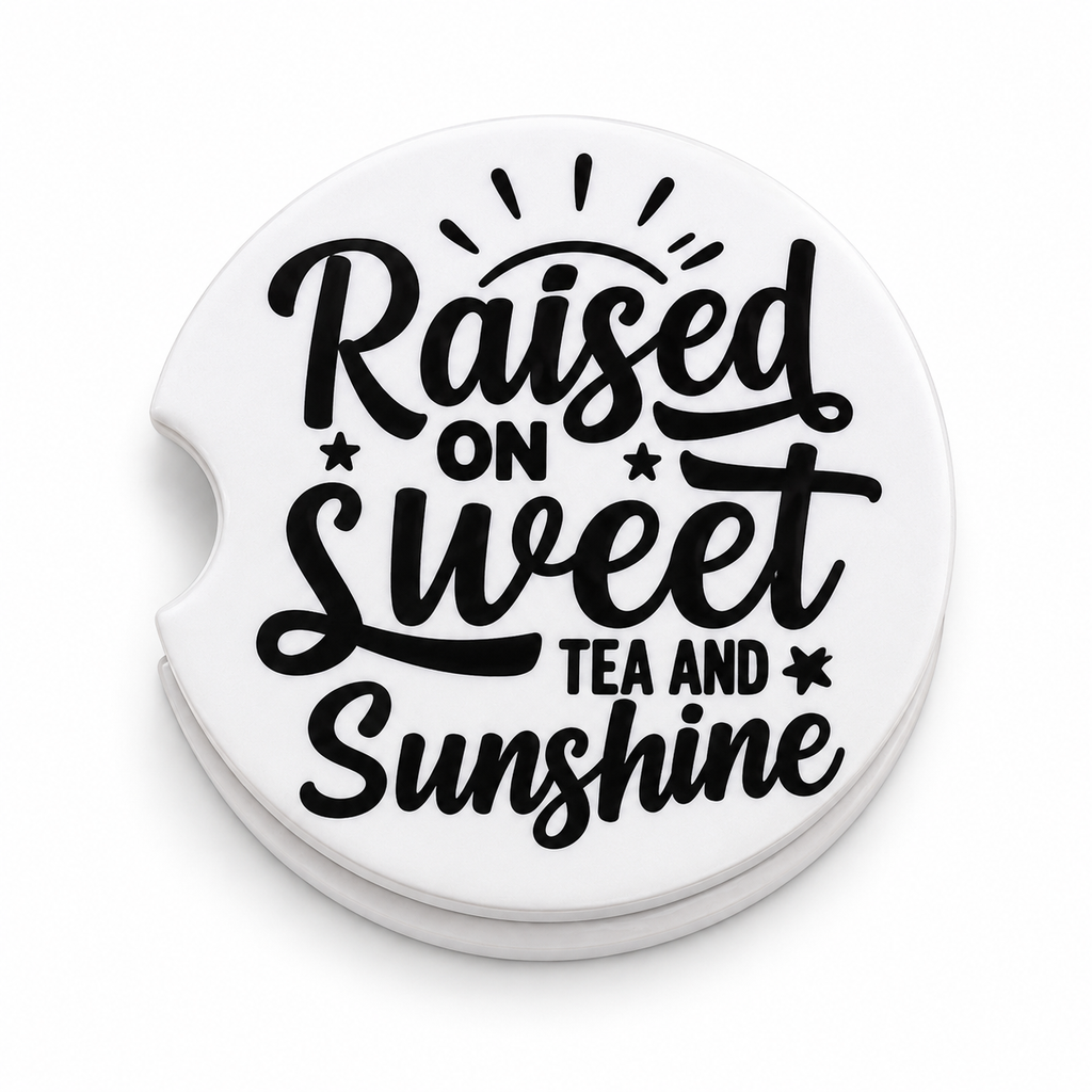 Close-up of Raised on Sweet Tea and Sunshine ceramic car coaster — bold black script lettering with sun rays and star accents on white background, finger notch visible
