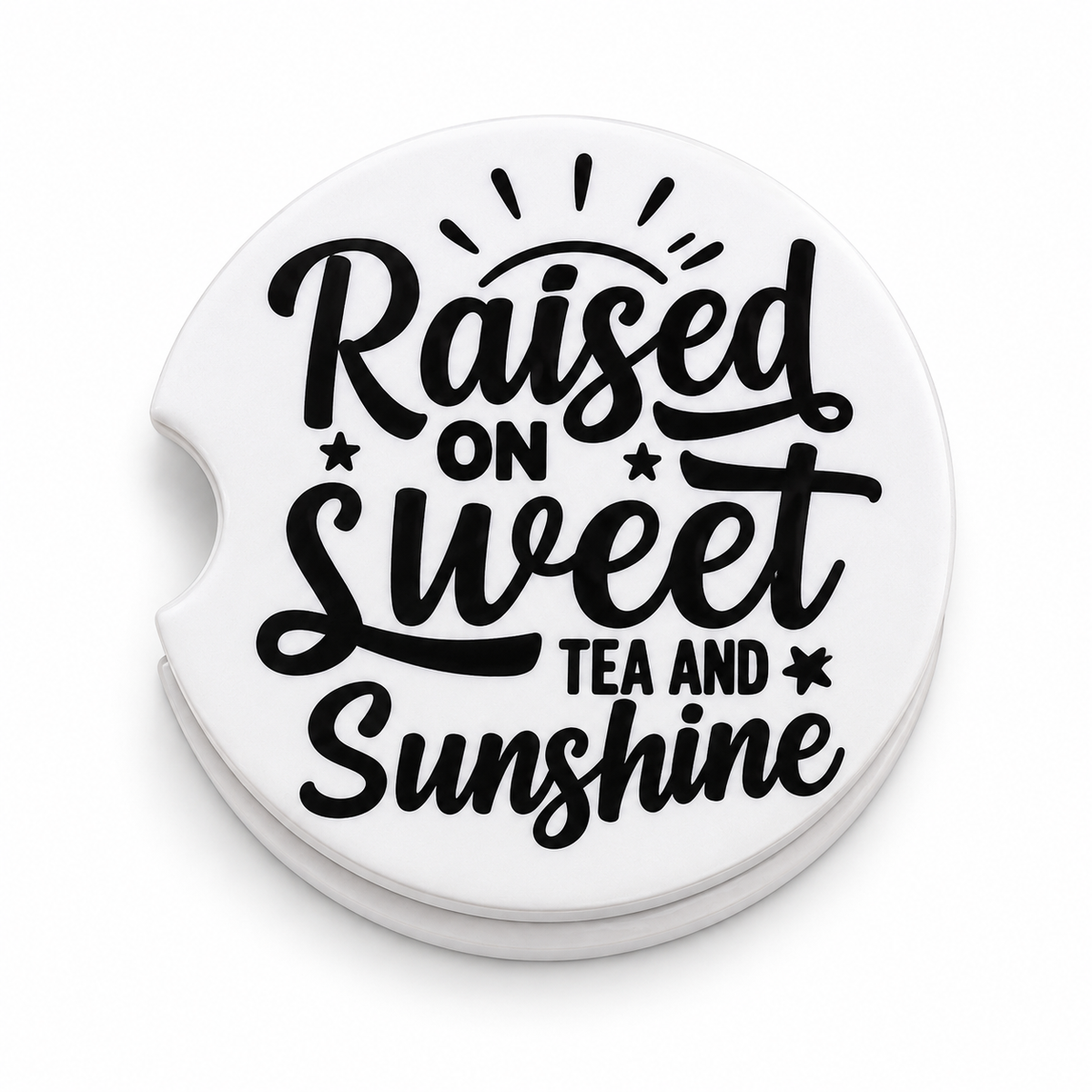 Close-up of Raised on Sweet Tea and Sunshine ceramic car coaster — bold black script lettering with sun rays and star accents on white background, finger notch visible
