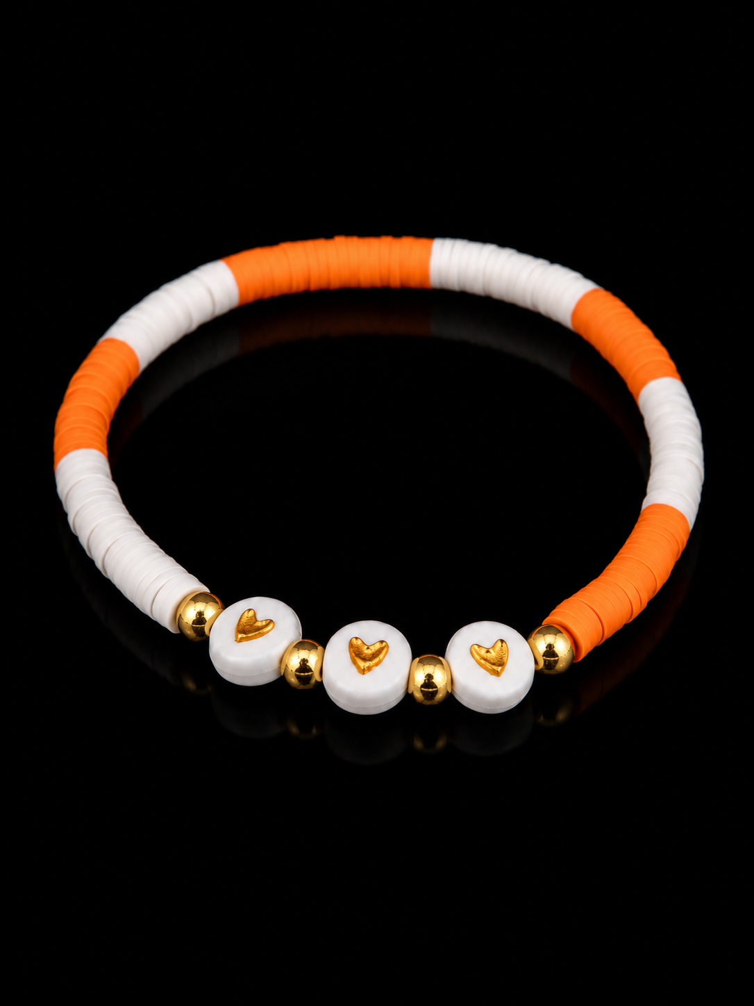 Orange and white beaded bracelet with gold heart accents shown at an angle on black reflective surface
