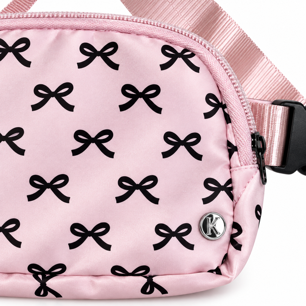 Close-up of Pink Bow Belt Bag and Crossbody showing all-over black bow print on pink nylon, silver Katydid K logo rivet, and black side-release buckle on adjustable pink satin strap
