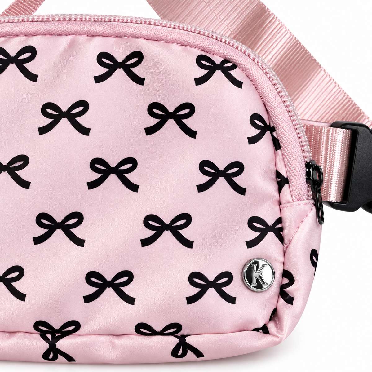 Close-up of Pink Bow Belt Bag and Crossbody showing all-over black bow print on pink nylon, silver Katydid K logo rivet, and black side-release buckle on adjustable pink satin strap

