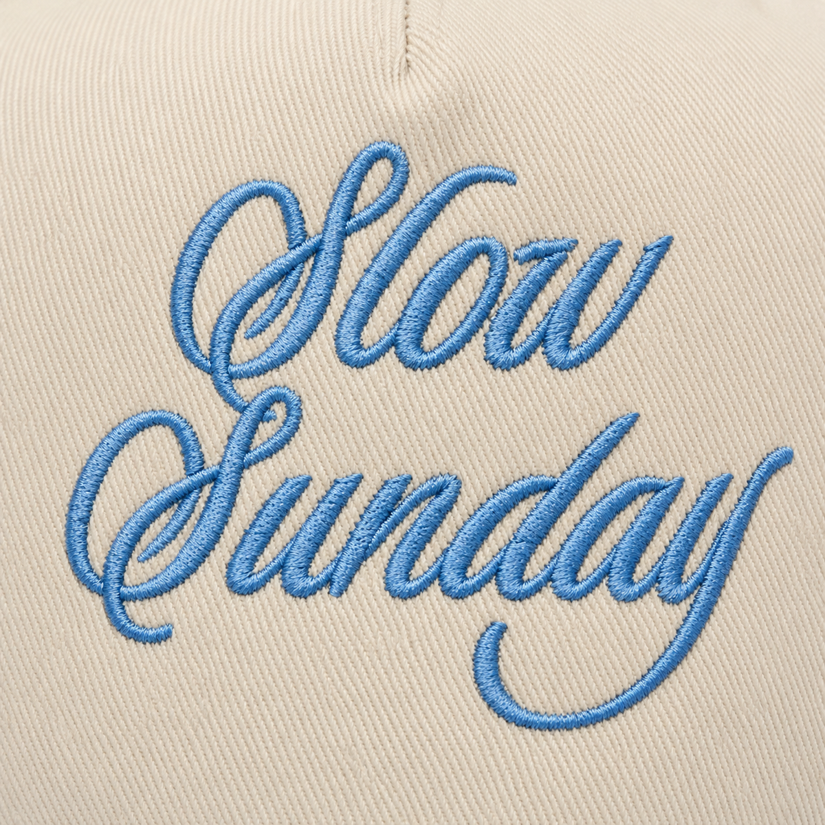 Close-up of light blue embroidered Slow Sunday script lettering on cream structured baseball cap crown
