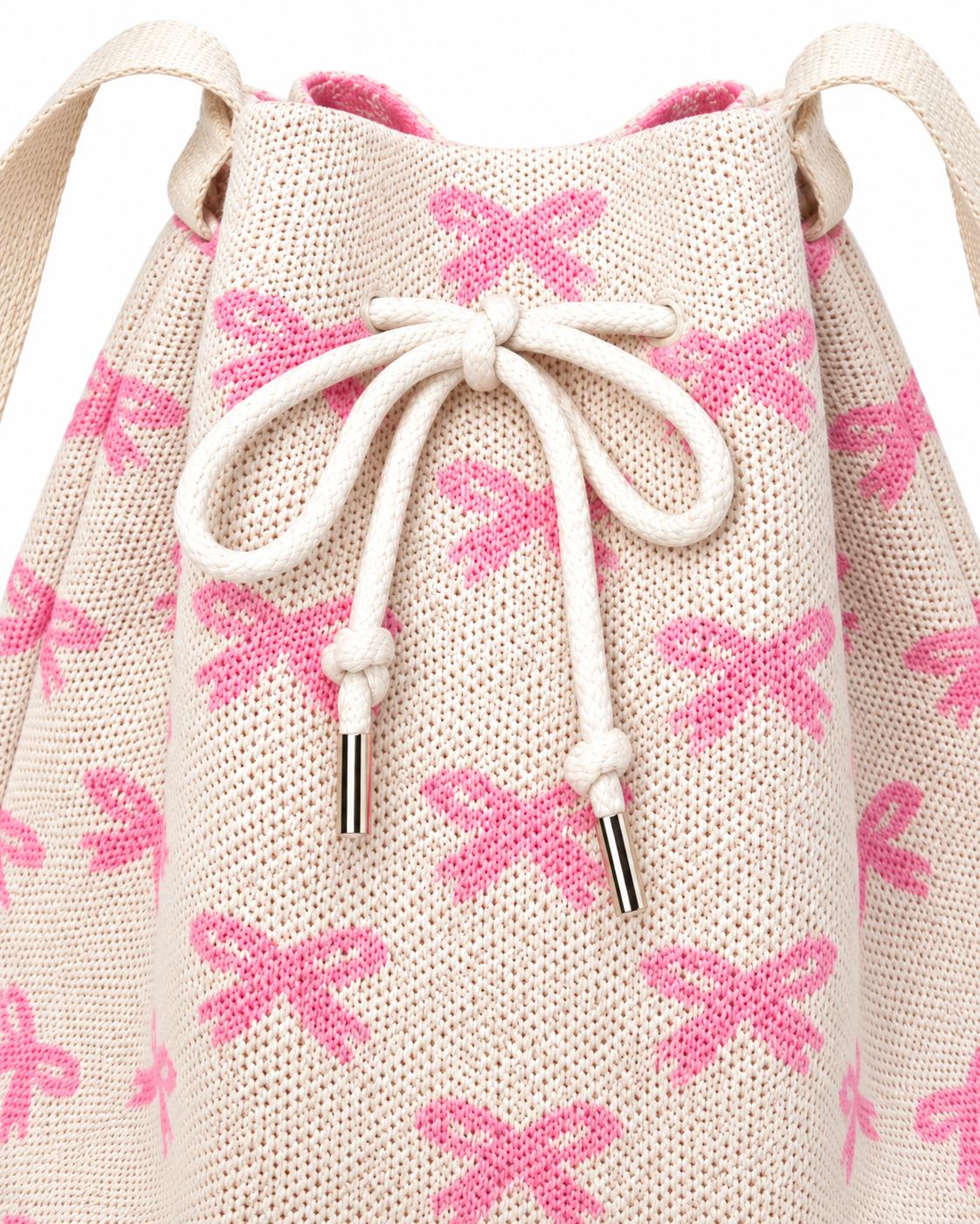 Close-up of Coquette Bow Crossbody Bucket Bag showing cream rope drawstring closure with silver aglet tips, woven pink bow pattern texture detail on cream knit fabric, and cream fabric strap attachment tabs on white background
