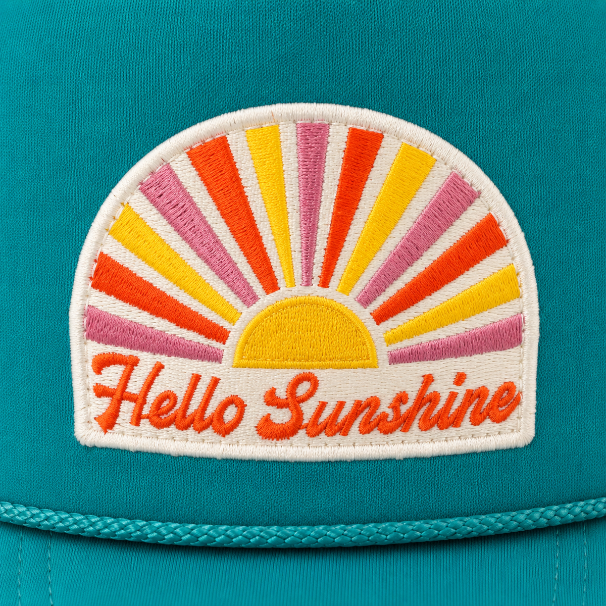 A close-up of a teal cap featuring a colorful embroidered patch with a semi-circular sunburst and the words 'Hello Sunshine' in orange script.