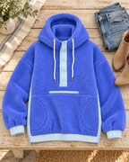 Blue two-toned sherpa pullover hoodie laid flat on a wooden table beside jeans and tan ankle boots, showing light blue trim and front pockets
