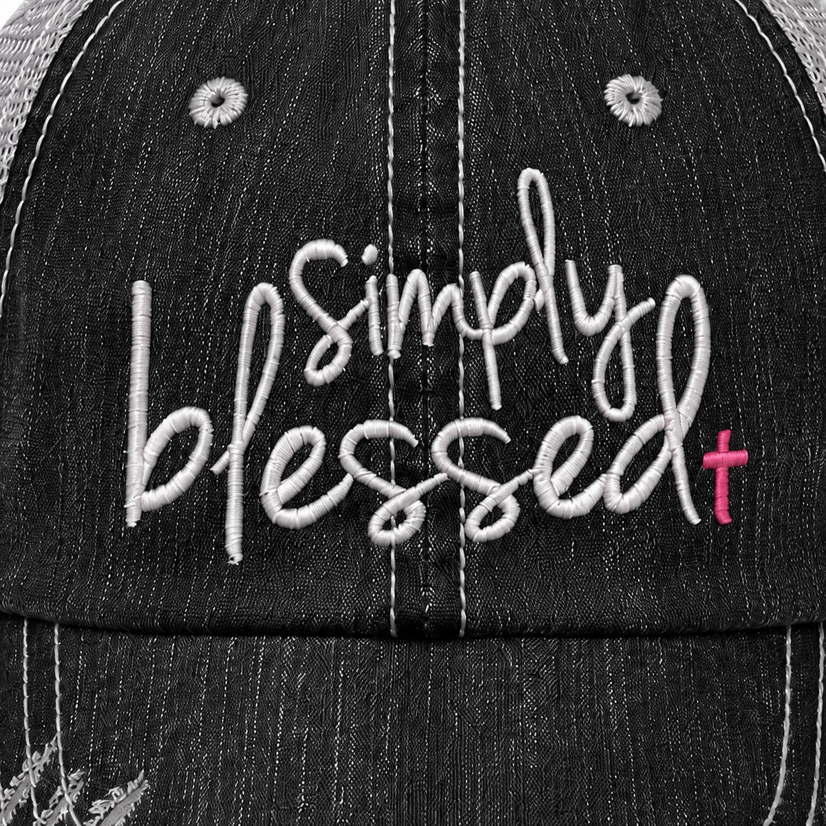 Close-up of a black denim-textured baseball cap with white embroidered script reading 'simply blessed' and a small pink cross accent on the right side.