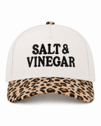 Salt & Vinegar Two-Tone Baseball Cap in Leopard front view showing cream structured cotton crown with bold black embroidered Salt & Vinegar block lettering, tan and brown leopard print bill, and leopard print top button on white background
