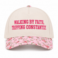 Walking By Faith Tripping Constantly Baseball Cap in Floral front view showing cream cotton crown with hot pink embroidered Walking By Faith Tripping Constantly block lettering, pink floral bill with red roses and green leaves, and pink floral top button on white background
