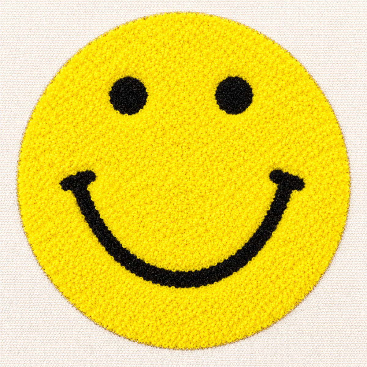 Close-up of large textured punch needle yellow smiley face with black embroidered round eyes and curved smile on natural canvas tote bag
