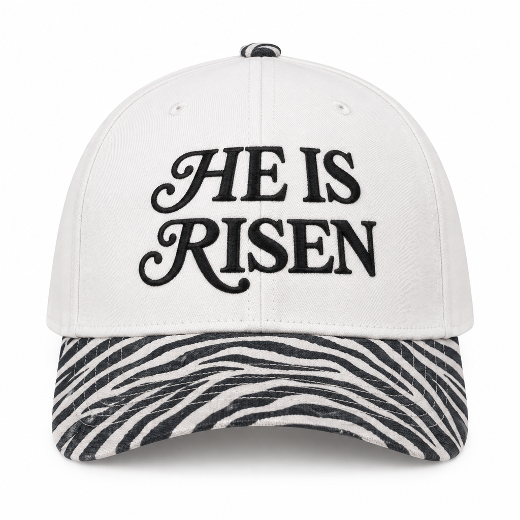 He Is Risen Baseball Cap in Zebra front view showing white cotton crown with black decorative script He Is Risen embroidery, black and white zebra print bill, and zebra print top button on white background
