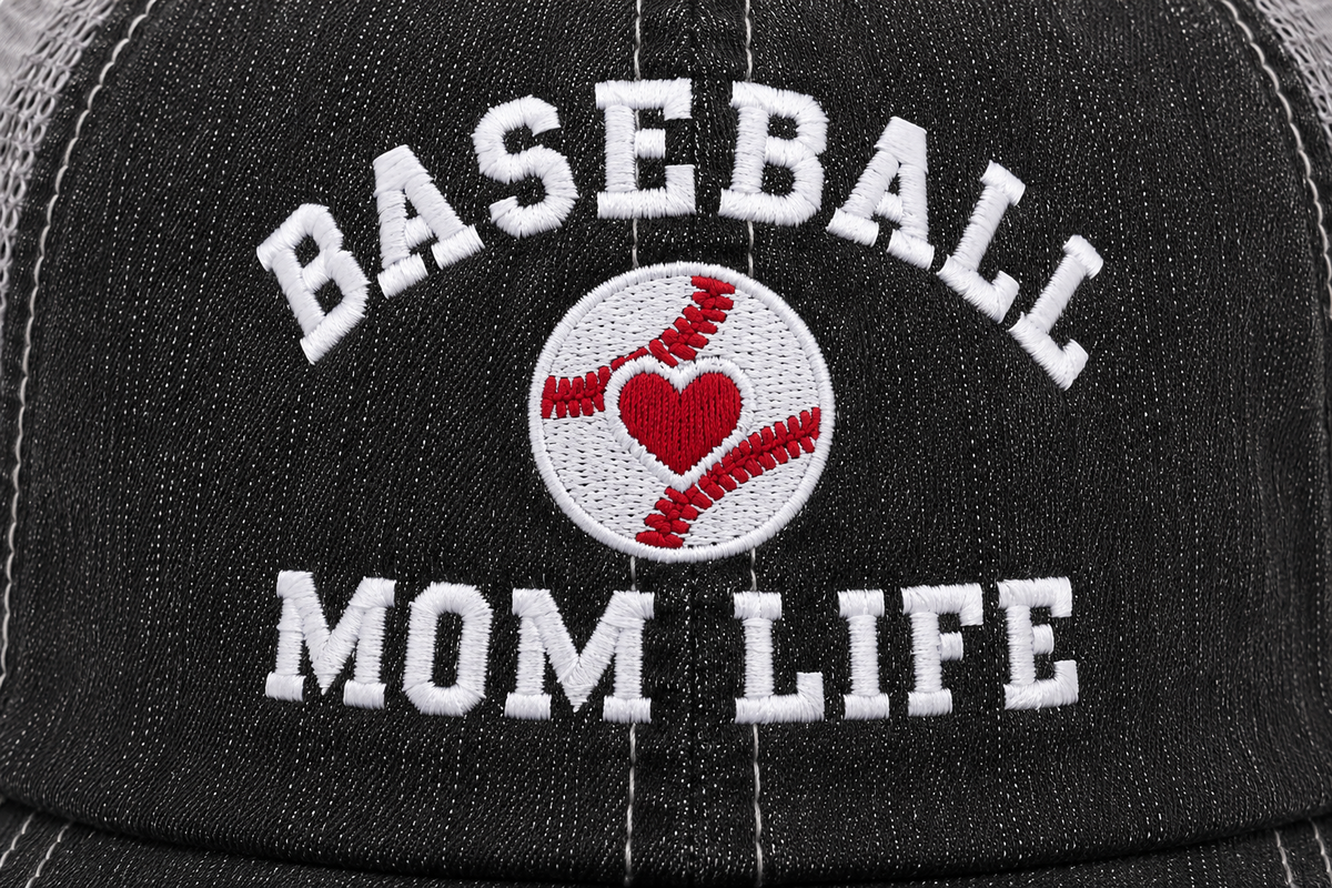 Close-up of embroidered Baseball Mom Life text on a distressed black trucker hat with a white baseball and red heart accent patch in the center.