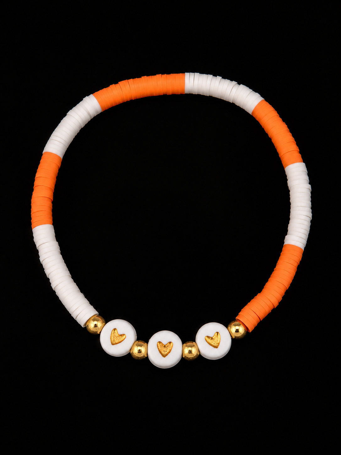 Orange and white heishi bead stretch bracelet with three white heart disc beads and gold-tone accents on black background
