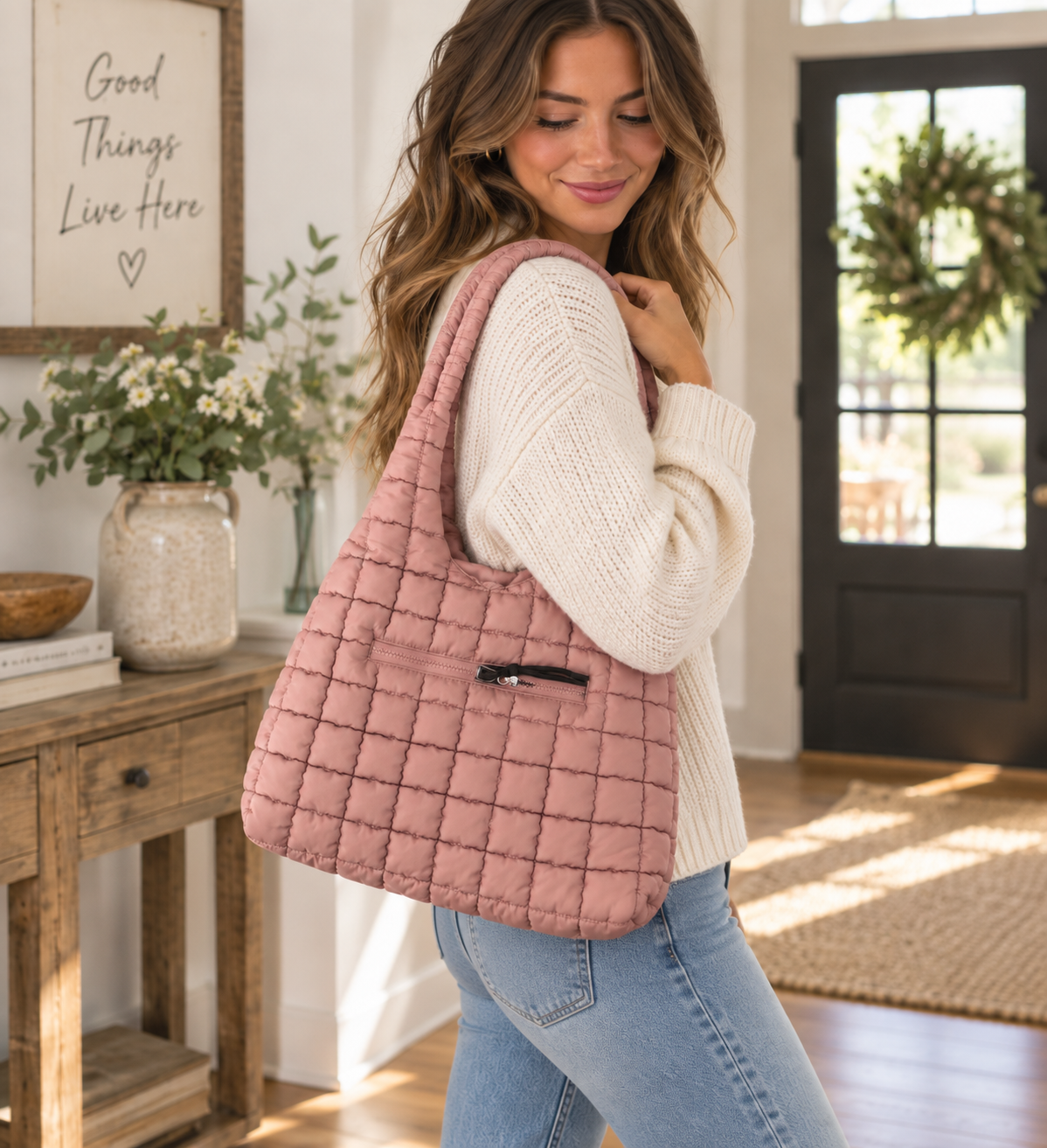 Woman carrying Mauve Quilted Tote Bag on shoulder showing soft mauve puffer quilted body, padded loop handle, and front zippered pocket with cream sweater and jeans in bright farmhouse interior
