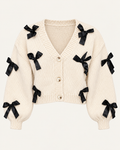 Front view of the tan cropped cardigan showing black ribbon bows, a ribbed V-neckline, three front buttons, and long sleeves
