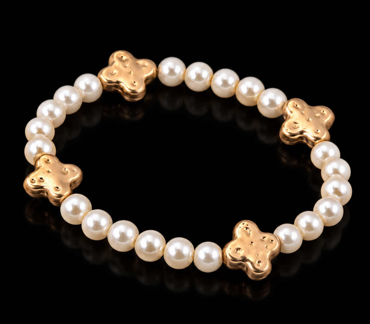 Pearl bead stretch bracelet with hammered gold-tone clover accents shown at an angle on black reflective surface
