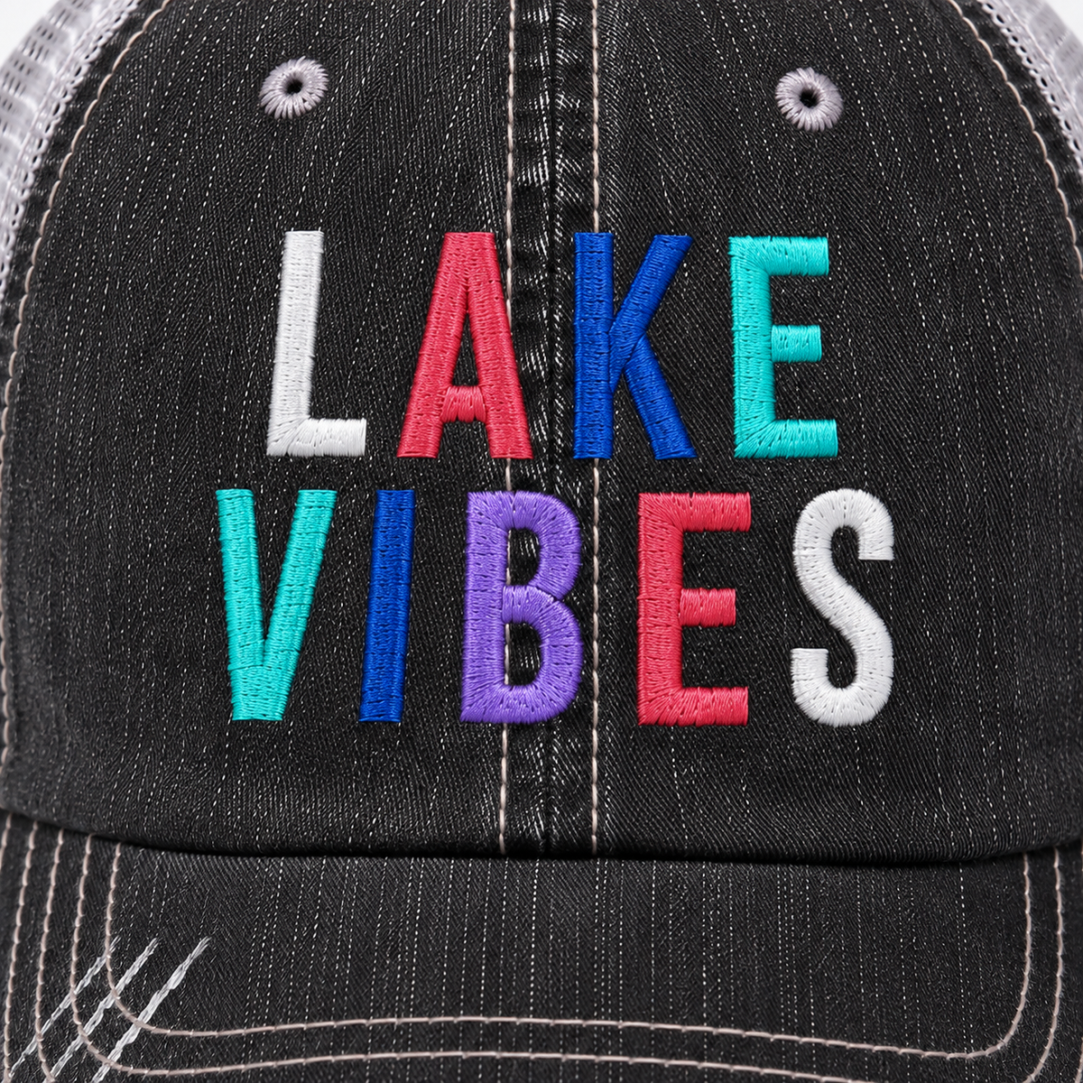 Close-up of Lake Vibes trucker hat showing colorful embroidered lettering and distressed black denim detail.