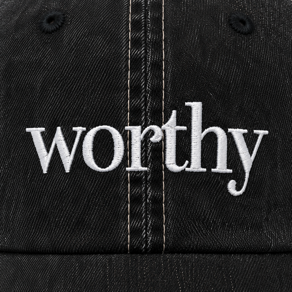  Close-up of white Worthy embroidery on the black denim front of the trucker hat.
