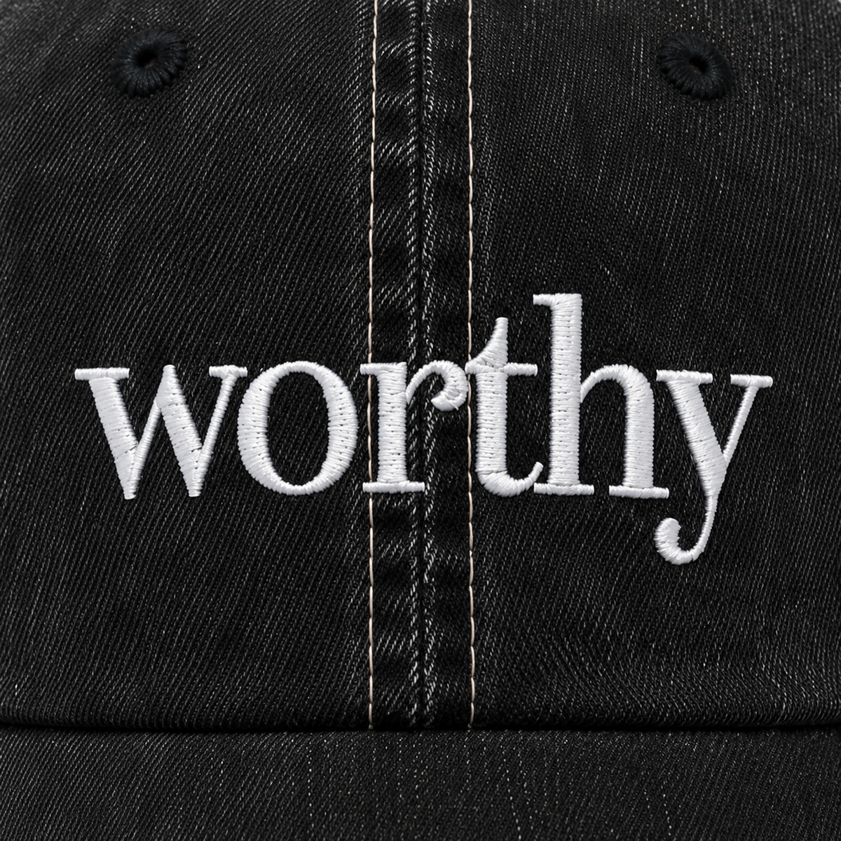  Close-up of white Worthy embroidery on the black denim front of the trucker hat.