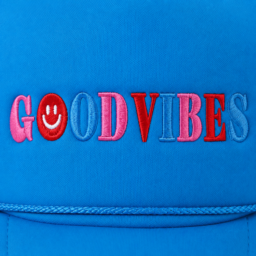 Close-up of multicolor embroidered "Good Vibes" lettering in pink, red, and periwinkle with a red smiley face accent on a bright sky blue trucker hat foam front panel with rope accent along the brim.
